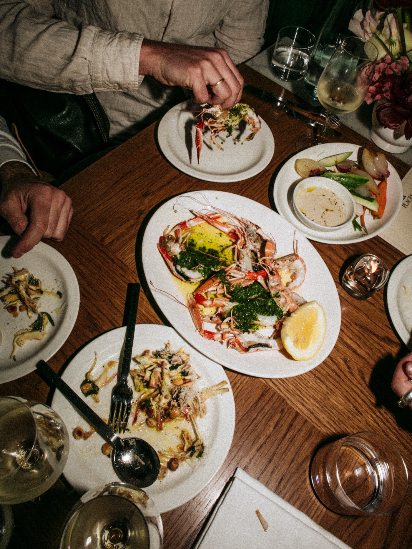 Overhead of a shared table — grilled langoustines with salsa verde, crudites and wine
