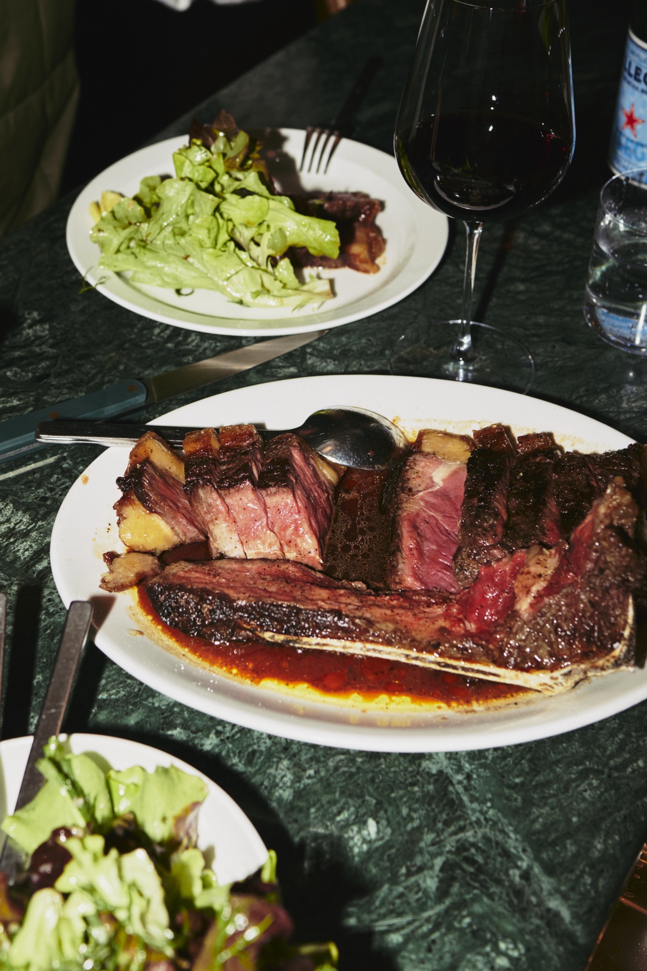 Sliced steak with salad and red wine on the green marble table
